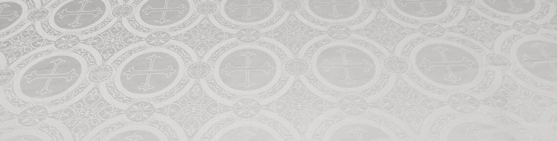 A close-up view of white liturgical brocade fabric featuring an intricate pattern of woven crosses and floral motifs